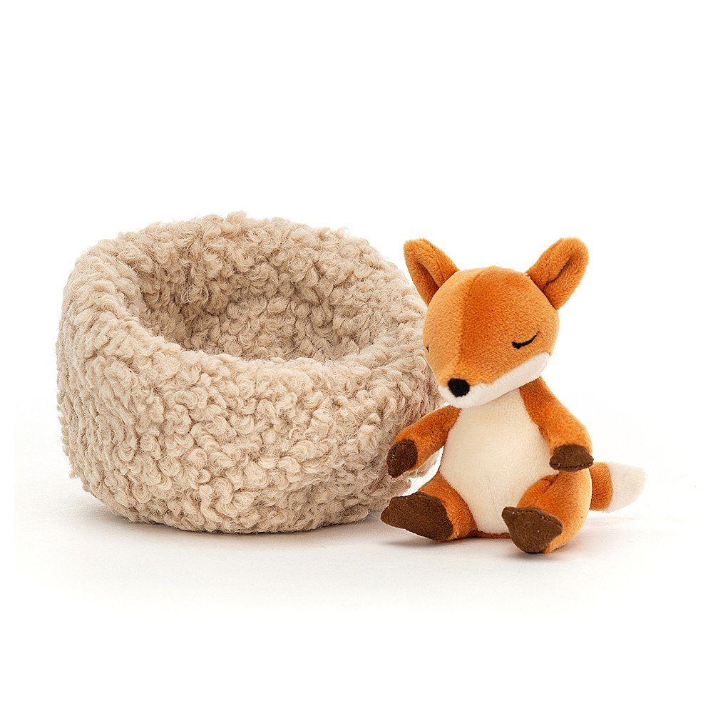 little jellycat fox sitting next to his cream beige cushion bed