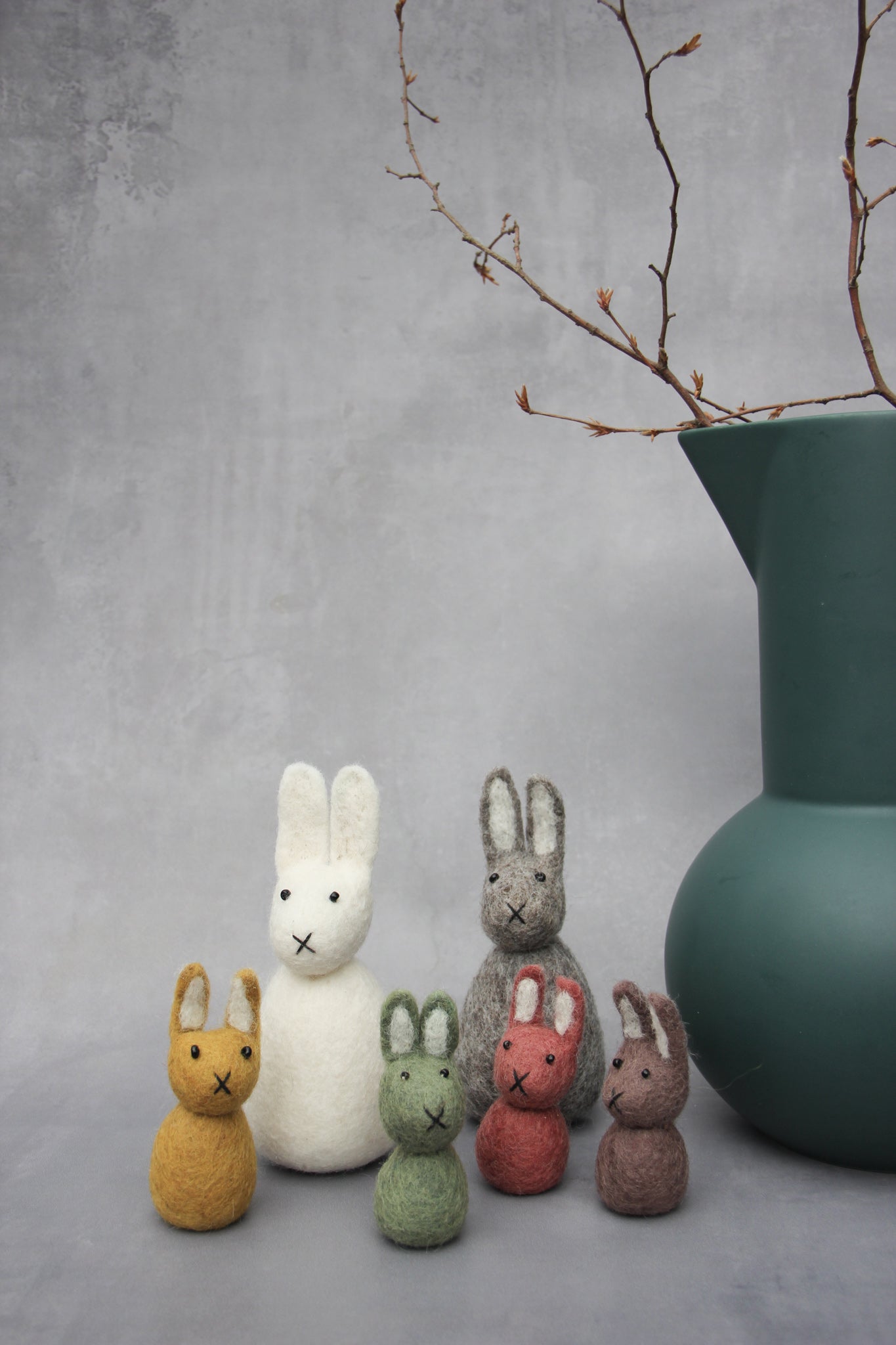 en gry & sif ochre, green, brown and red bunnies standing in a group next to a vase