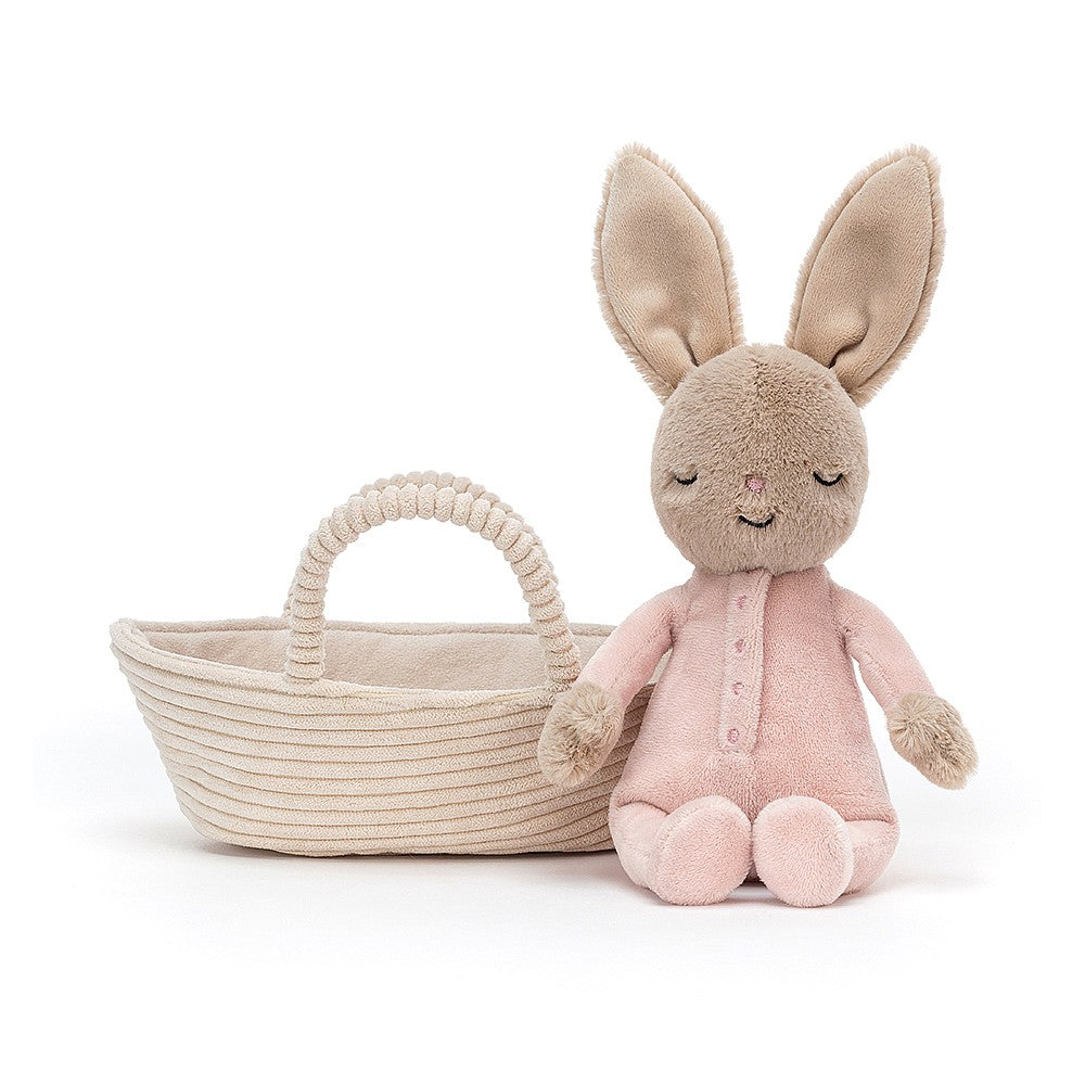 jellycat little bunny in pink babygrow sitting next to her little soft cream cradle