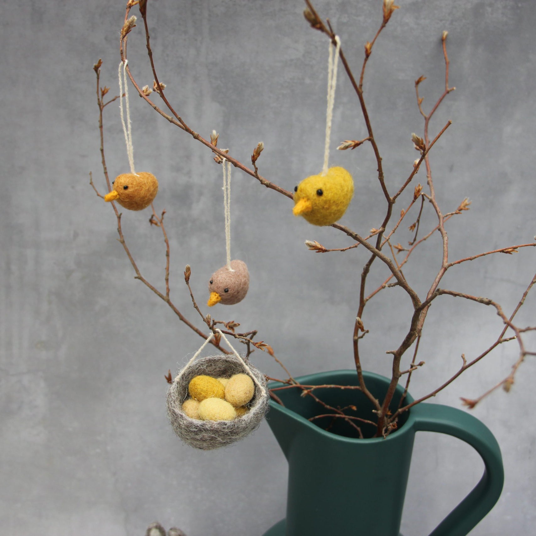 En Gri & Sif Felt birds hanging on twigs with a little hanging grey nest with eggs